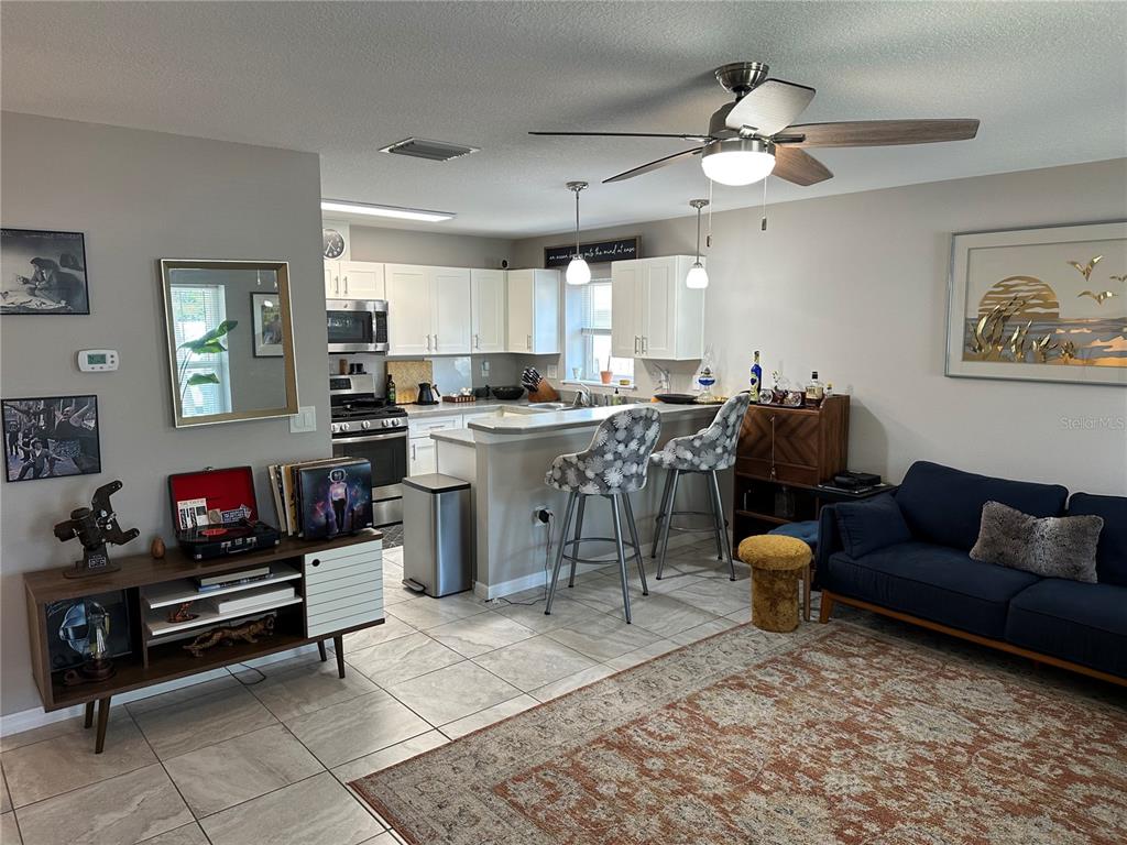 An open-concept living room and kitchen featuring tile floors, a breakfast bar, and white cabinetry — 1119 BEVERLY AVENUE, LARGO, FL