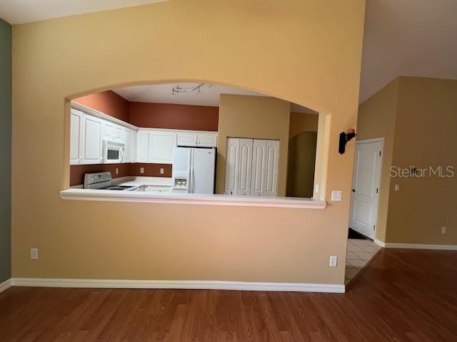 A view through an arched opening into a kitchen with white cabinets and wood flooring — 77 VERANDA WAY, PALM COAST, FL