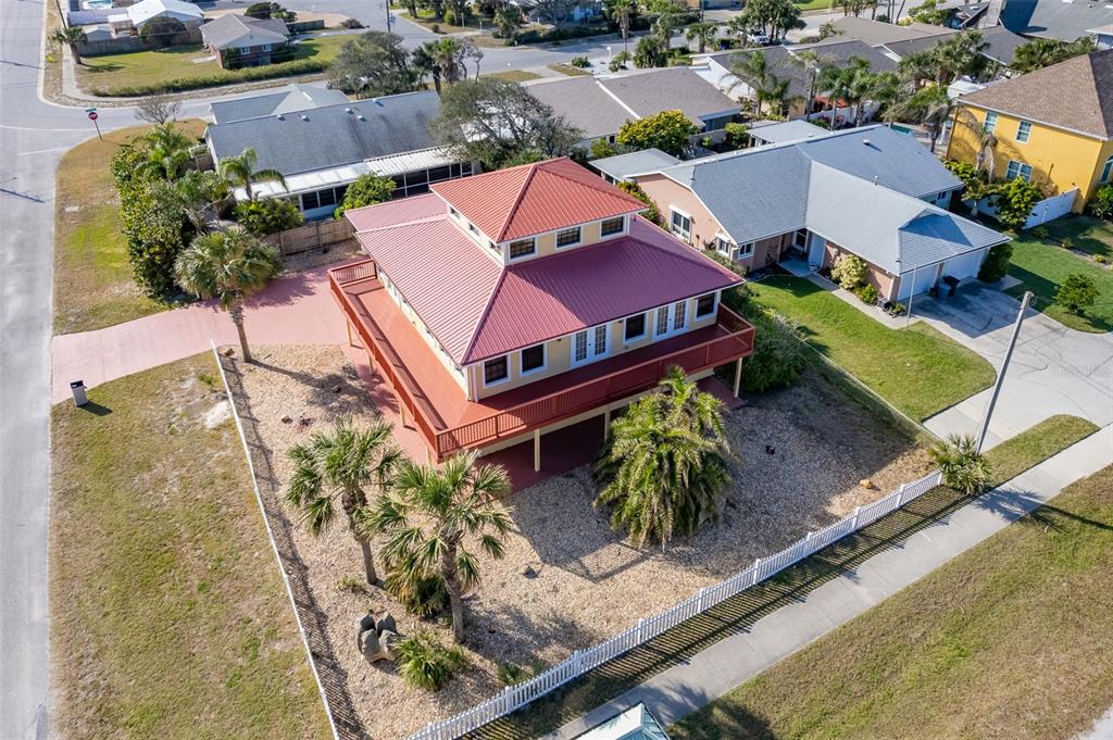 An elevated house with a red metal roof and wraparound deck sits on a corner lot — 3726 S ATLANTIC AVENUE, NEW SMYRNA BEACH, FL