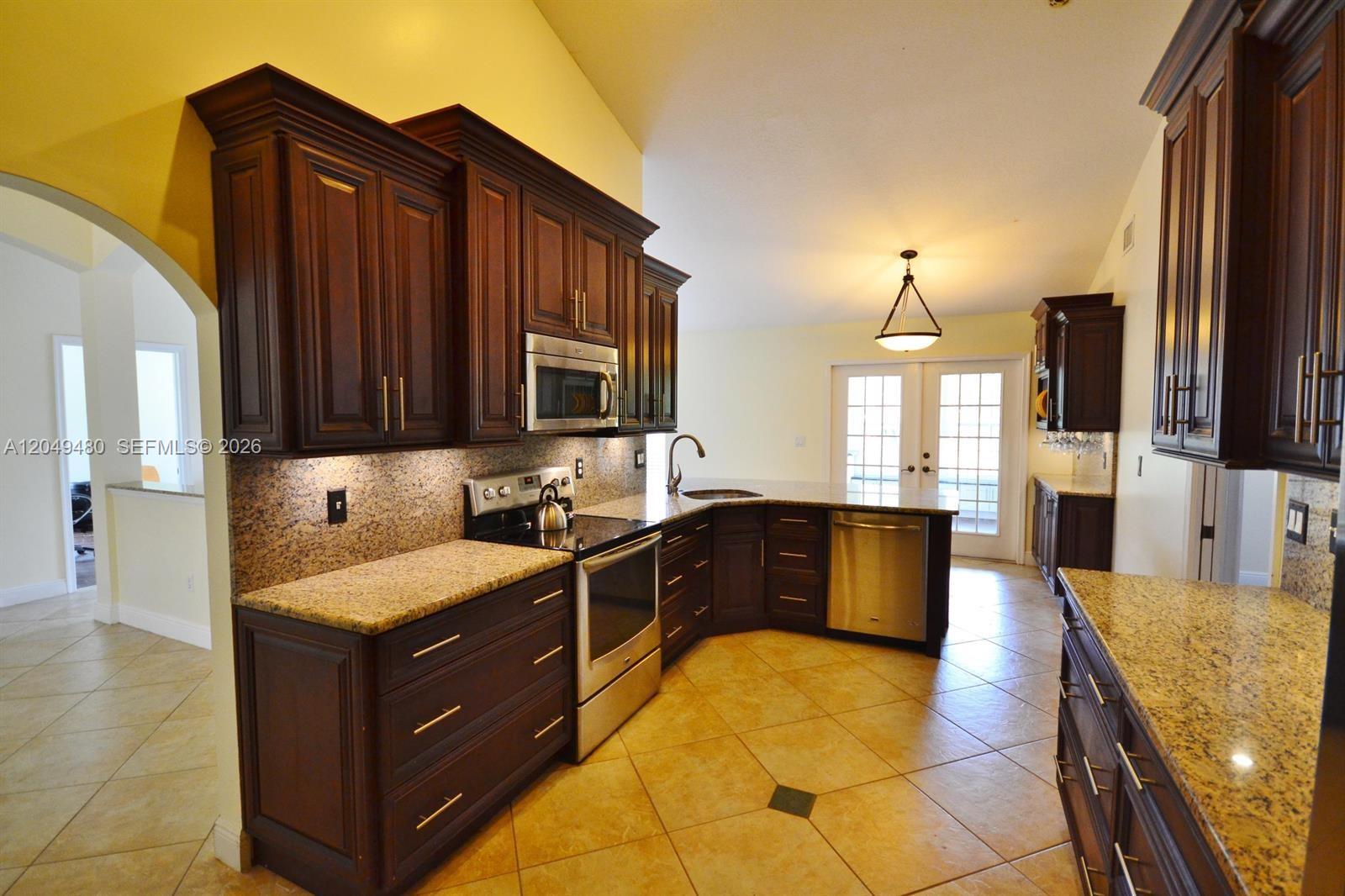 A kitchen features dark wood cabinets, granite countertops, stainless steel appliances, and tile flooring — 17569 N 89th Pl N, Loxahatchee FL 33470, LOXAHATCHEE, FL