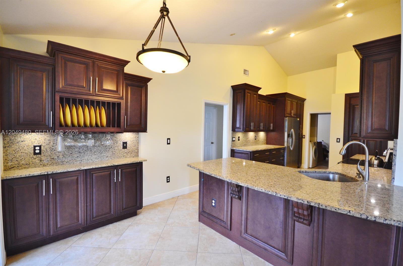 A kitchen features dark wood cabinetry, granite countertops, a central island, and tile flooring — 17569 N 89th Pl N, Loxahatchee FL 33470, LOXAHATCHEE, FL