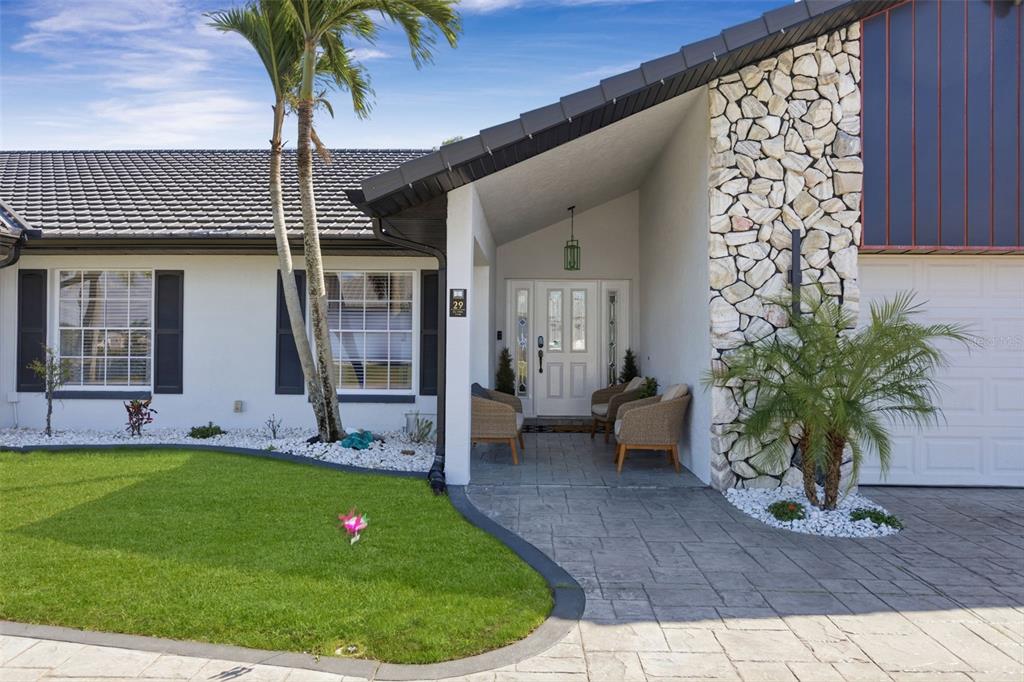 A white house exterior features a stone-accented facade, a covered entryway, and a paved driveway — 29 SE 10TH AVENUE, CAPE CORAL, FL