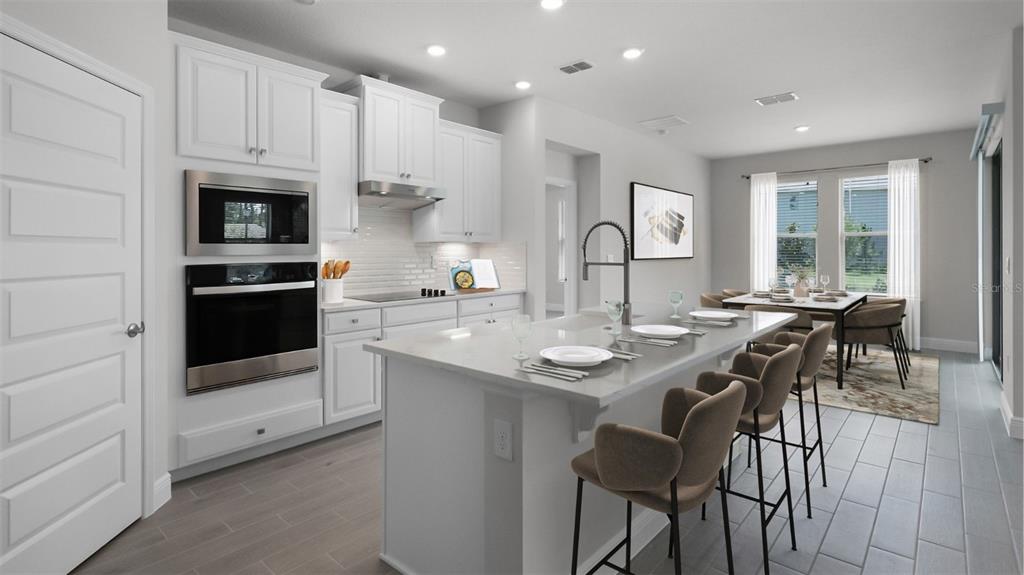 A modern kitchen features white cabinetry, a central island with bar seating, and tile flooring — 11253 HOLLOW BAY DRIVE, WINTER GARDEN, FL