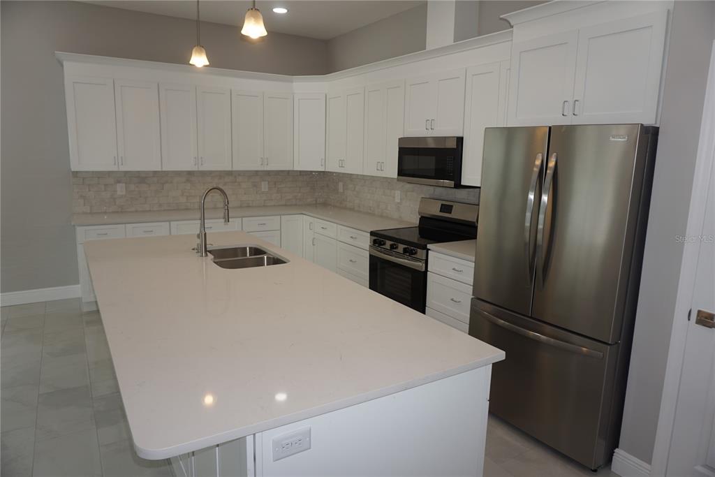 A modern kitchen features white cabinetry, stainless steel appliances, and a large quartz-topped island — 12572 TREE STREET, LARGO, FL