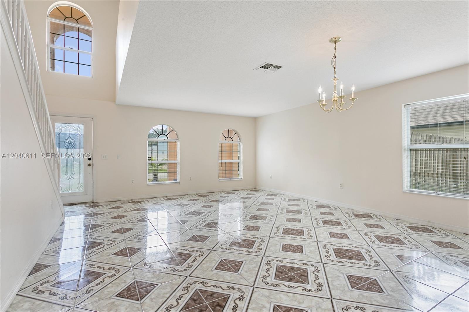 A bright, empty living room features patterned tile floors, arched windows, and a chandelier — 12096 Prospect Creek Dr # 0, Jacksonville FL 32218, JACKSONVILLE, FL