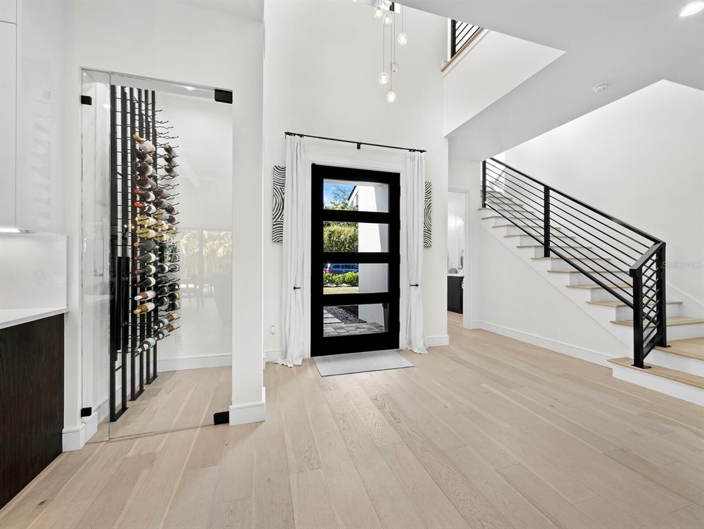 A modern entryway features light wood floors, a glass-enclosed wine rack, and a black staircase — 1717 ALTA VISTA STREET, SARASOTA, FL