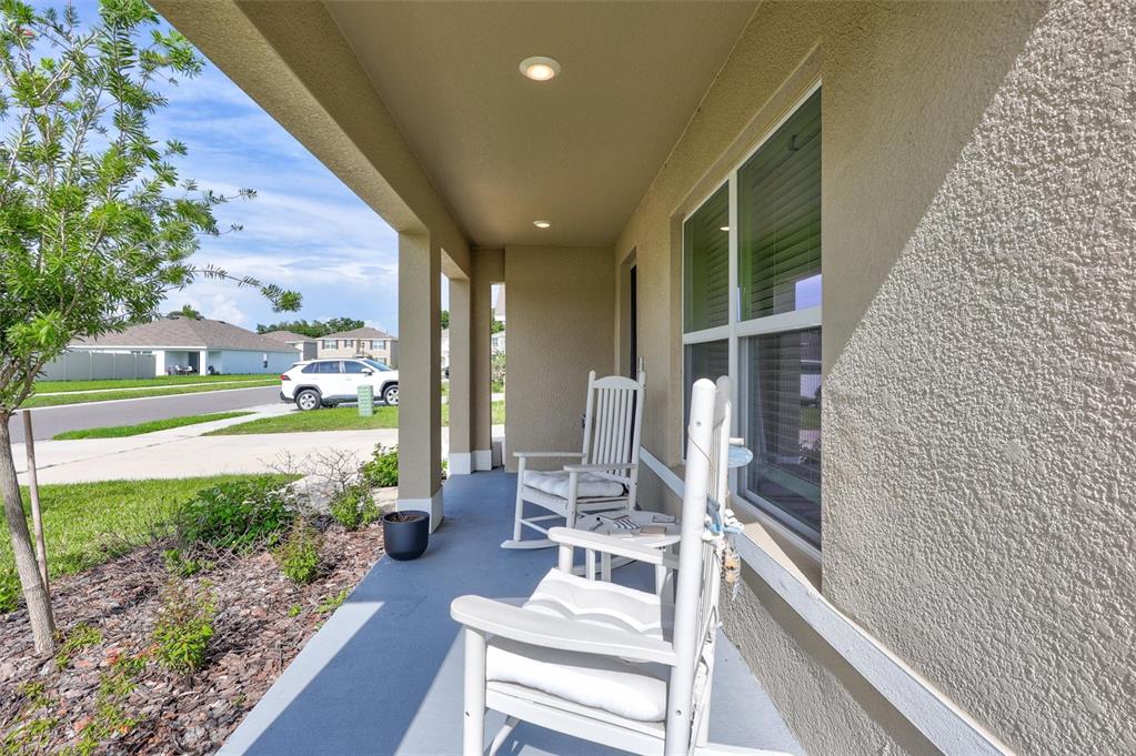 A covered front porch features two white rocking chairs and a view of the street — 7601 ROSEWOOD GARDEN LOOP, TAMPA, FL