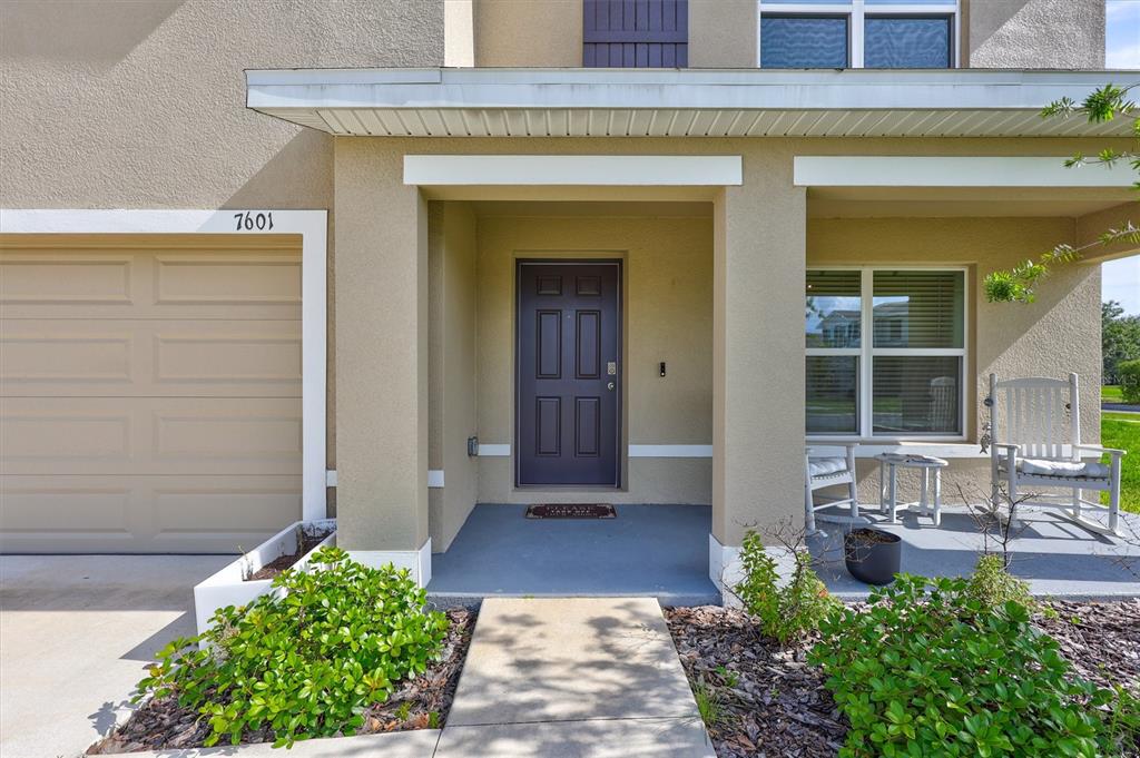 A front exterior view of a house with a garage, covered porch, and front door — 7601 ROSEWOOD GARDEN LOOP, TAMPA, FL