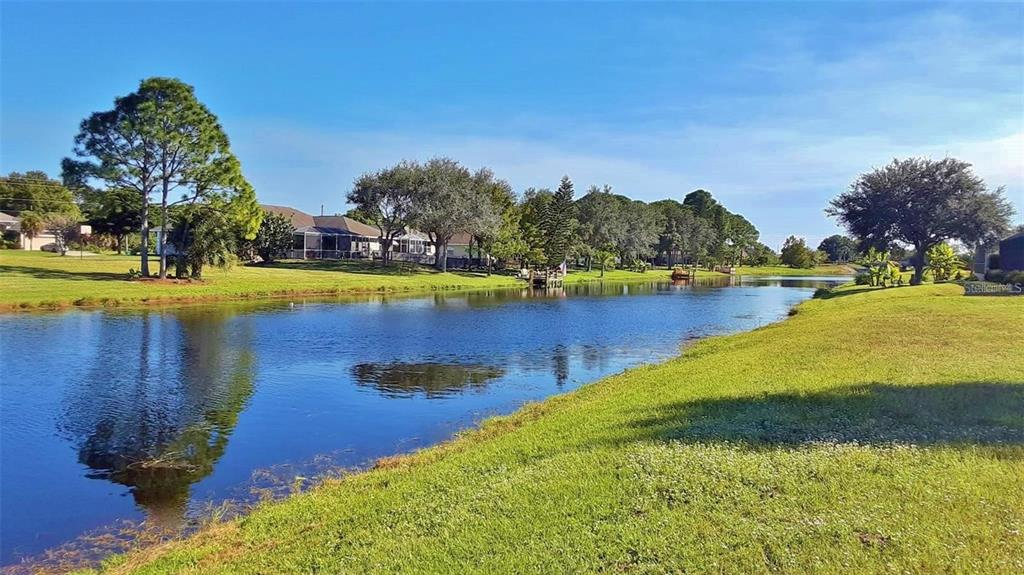 A grassy lawn slopes down to a calm pond with trees and houses in the background — 845 ROTONDA CIRCLE, ROTONDA WEST, FL