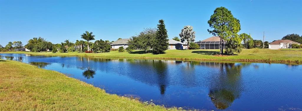 A calm pond sits in front of a grassy lawn with several houses and trees — 845 ROTONDA CIRCLE, ROTONDA WEST, FL