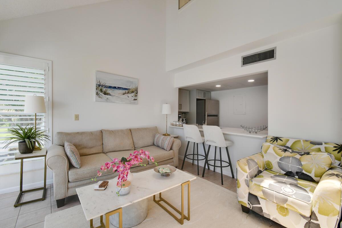 A living room features a beige sofa, patterned armchair, marble coffee table, and kitchen bar — 1605 S Us Highway 1 # 214, Jupiter FL 33477, JUPITER, FL
