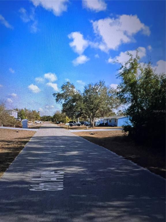 A paved road leads toward a residential area with houses and trees under a blue sky — 11409 8TH AVENUE, PUNTA GORDA, FL