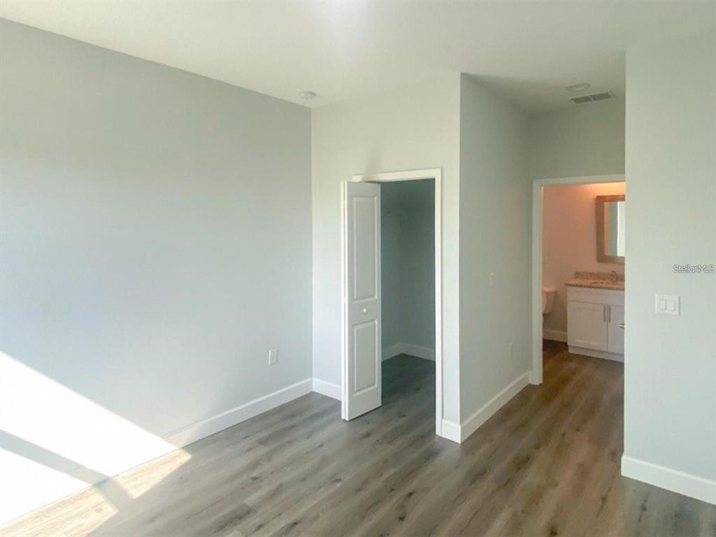 A bedroom with light gray walls, wood-look flooring, a closet, and an attached bathroom — 9163 AGATE STREET, PORT CHARLOTTE, FL