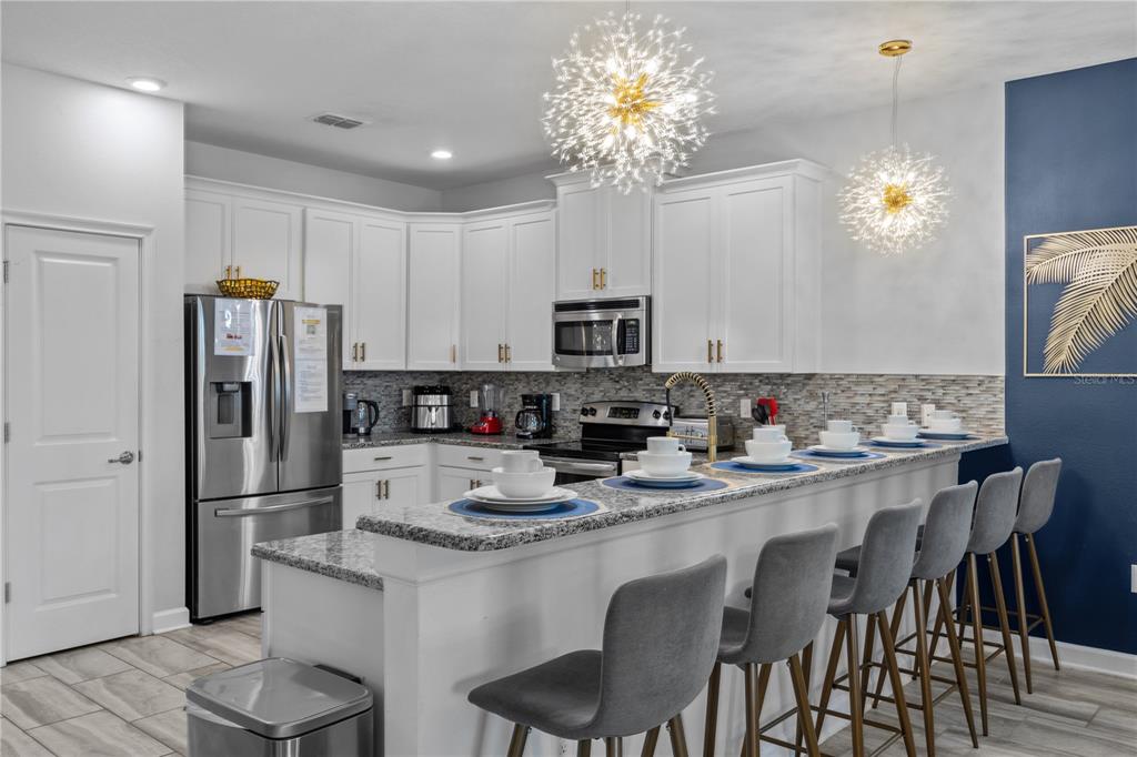 A kitchen with white cabinets, granite countertops, a breakfast bar, and two modern pendant lights — 1314 BIRDIE WAY, DAVENPORT, FL