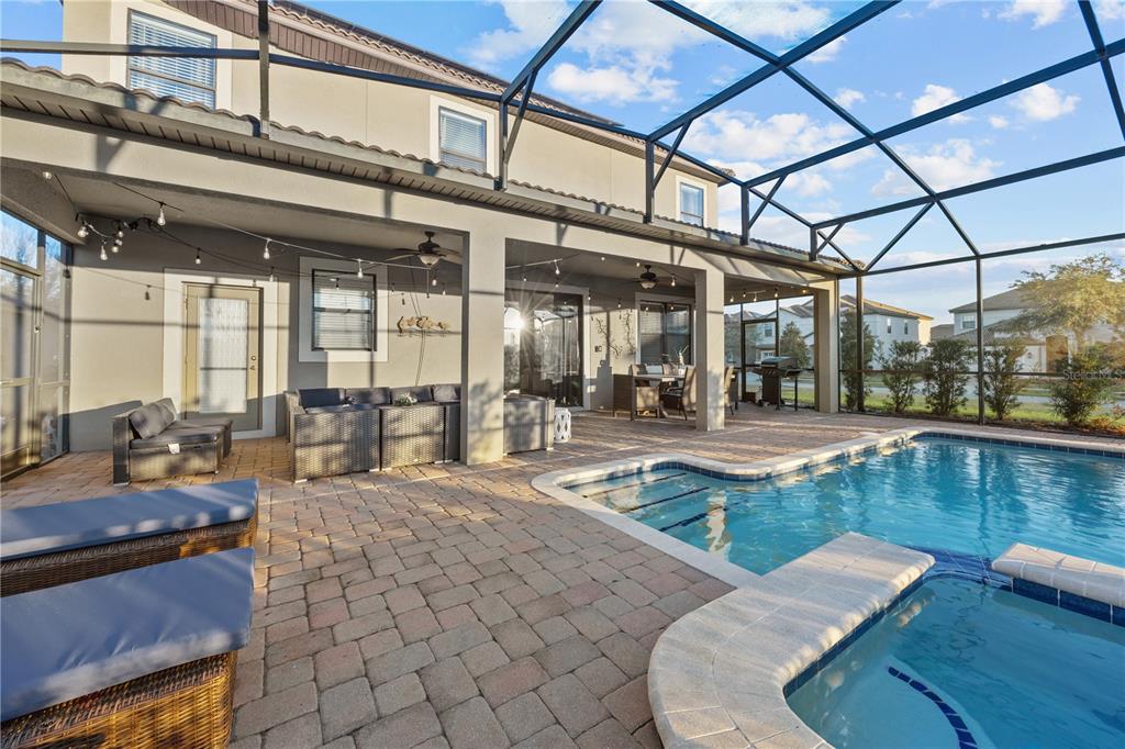 A covered patio with a pool, spa, and screened enclosure overlooks a residential backyard — 1314 BIRDIE WAY, DAVENPORT, FL