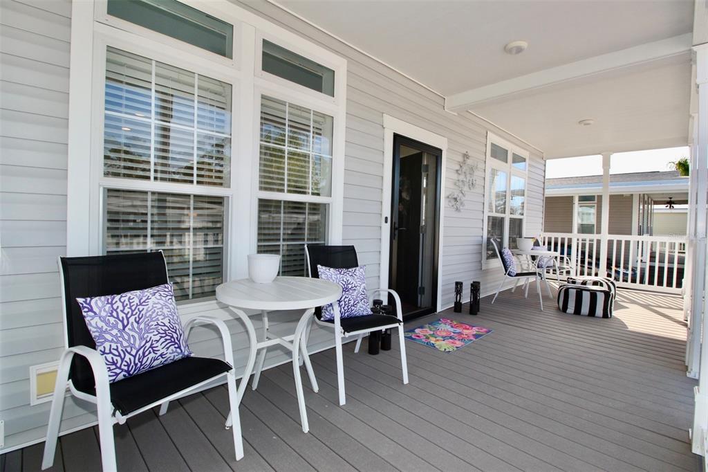 A covered porch with gray decking features outdoor seating, a small table, and large windows — 82107 A STREET N UNIT 107, PINELLAS PARK, FL