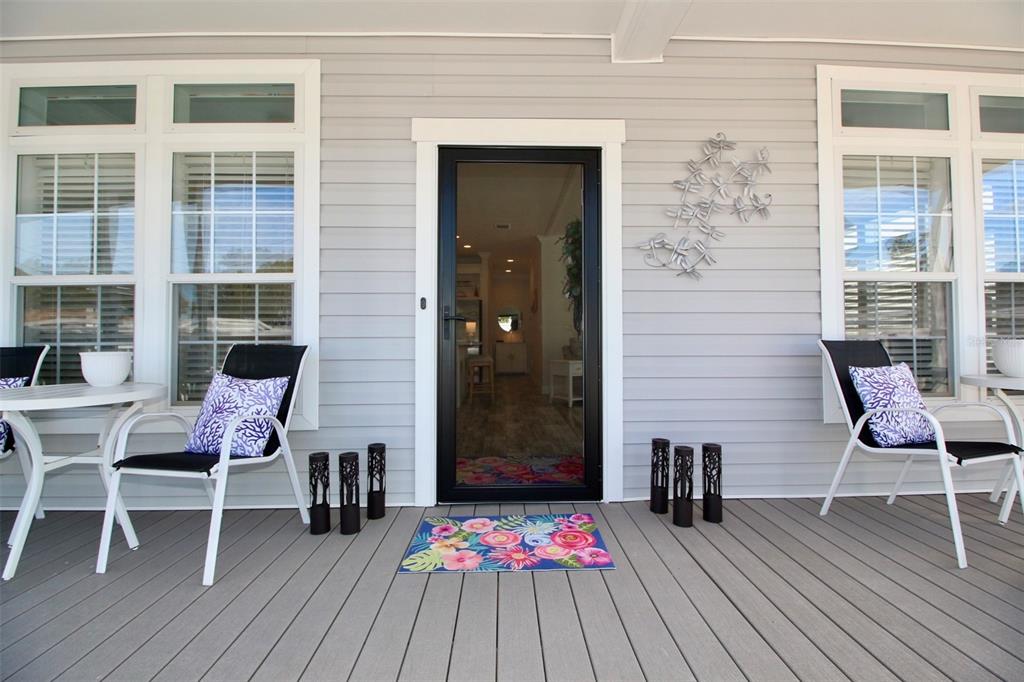 A gray-sided porch features a black screen door, two chairs with patterned pillows, and decor — 82107 A STREET N UNIT 107, PINELLAS PARK, FL