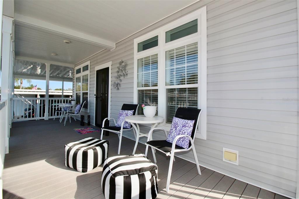 A covered porch features gray siding, a small table with two chairs, and two ottomans — 82107 A STREET N UNIT 107, PINELLAS PARK, FL