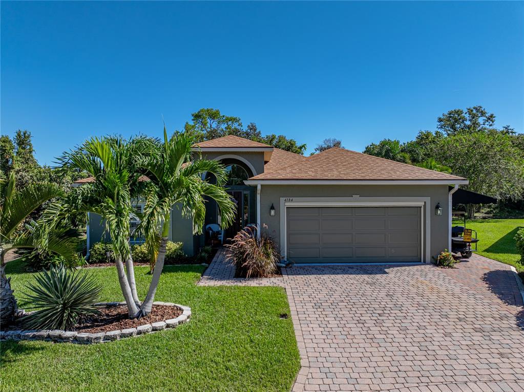 A single-story house with a tan stucco exterior, a brown shingled roof, and a paved driveway — 4184 ABERDEEN LANE, LAKE WALES, FL