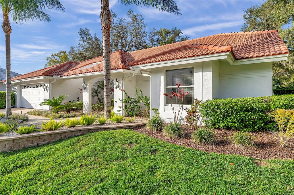 A single-story house with a white stucco exterior, orange tile roof, and landscaped front yard — 5473 BLUE HERON LANE, WESLEY CHAPEL, FL