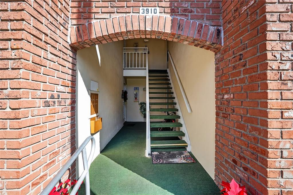 An exterior view shows a brick-arched entryway leading to a staircase and a green carpeted hallway — 3910 37TH STREET S UNIT 39, ST PETERSBURG, FL