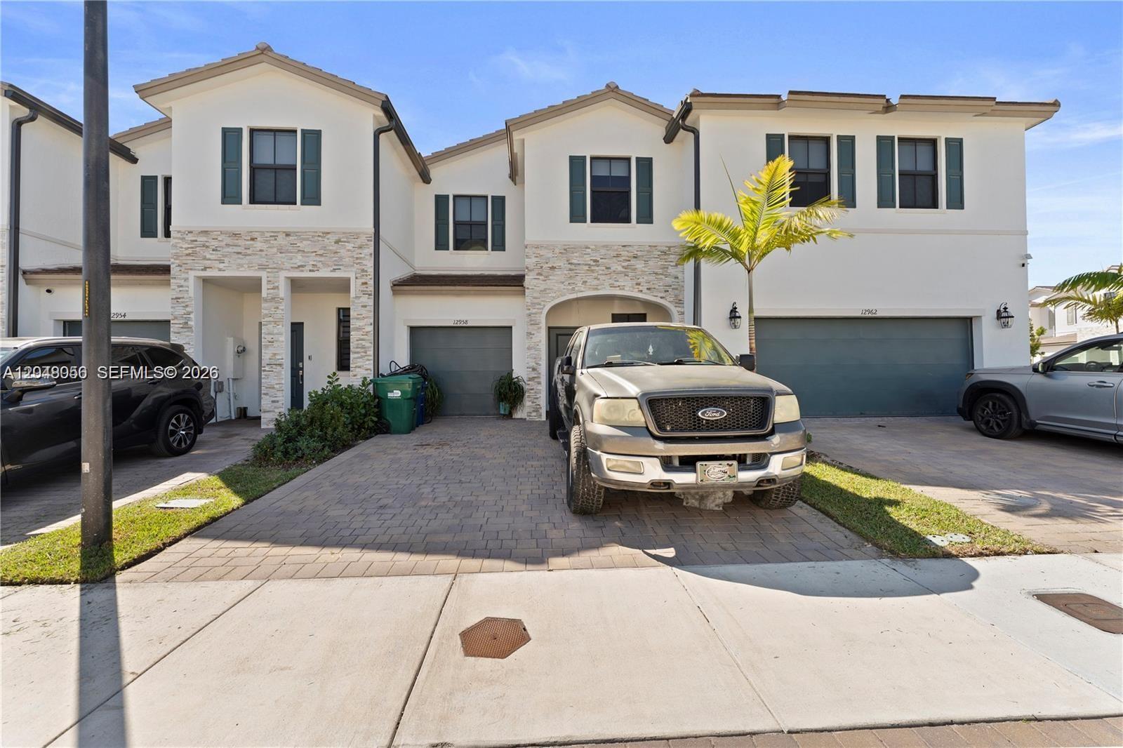 A multi-unit residential building features white stucco facades, stone accents, and paved driveways with parked vehicles — 12958 SW 231st St, Miami FL 33170, MIAMI, FL