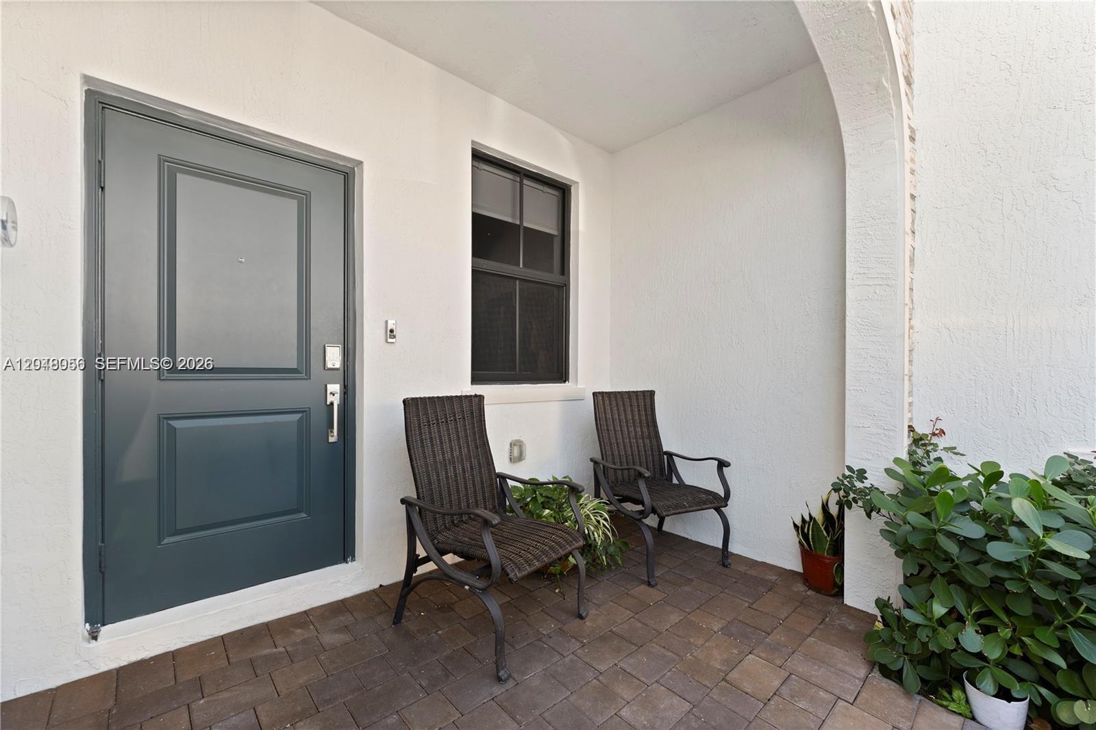A covered patio features a dark gray door, a window, and two wicker chairs — 12958 SW 231st St, Miami FL 33170, MIAMI, FL