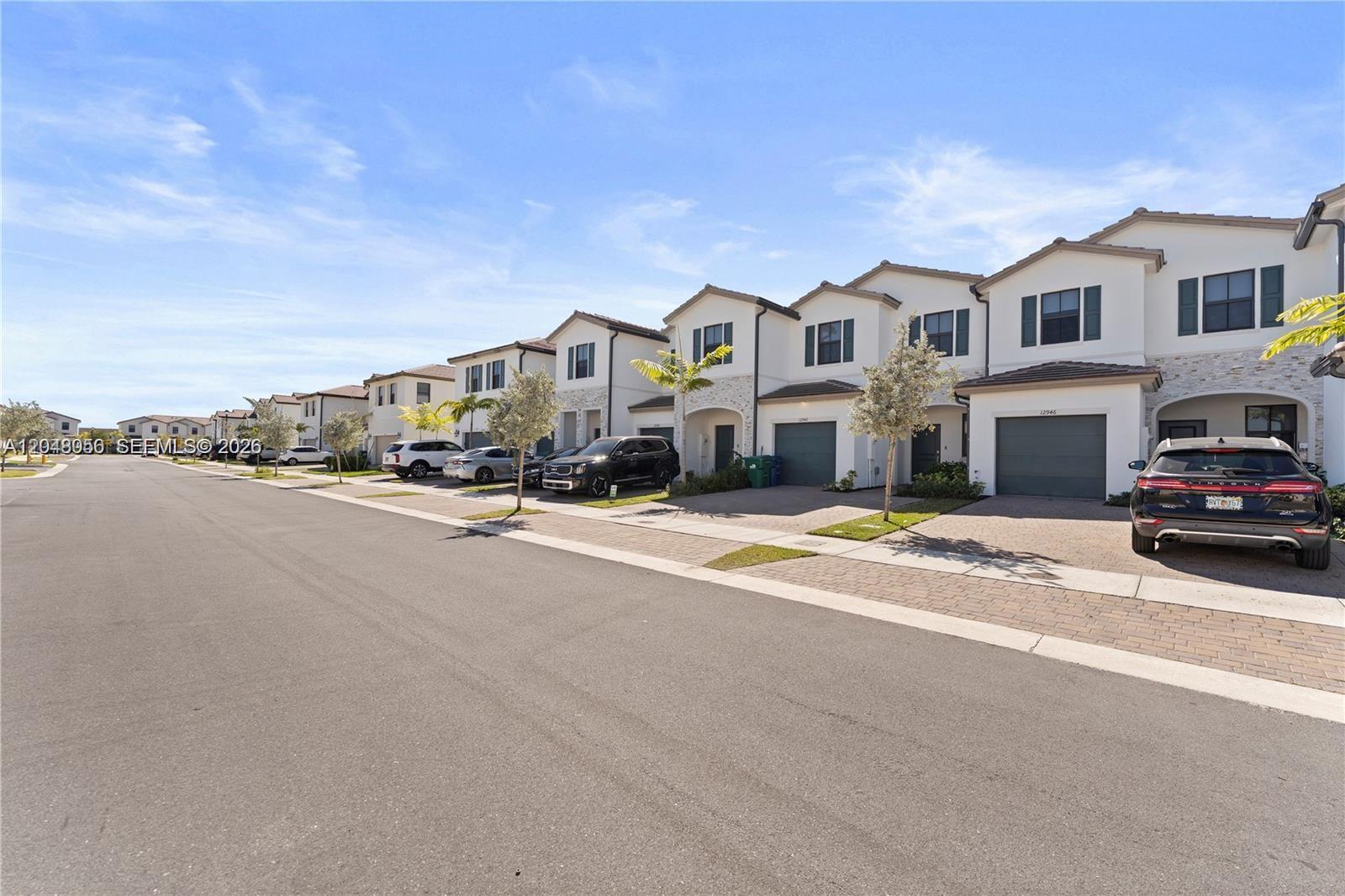A row of two-story townhouses with attached garages and paved driveways under a blue sky — 12958 SW 231st St, Miami FL 33170, MIAMI, FL