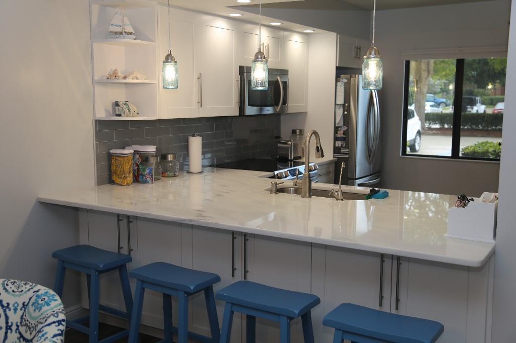 A kitchen features white cabinets, a marble-look countertop, blue bar stools, and gray subway tile — 901 Seafarer Circle # 101, Jupiter FL 33477, JUPITER, FL
