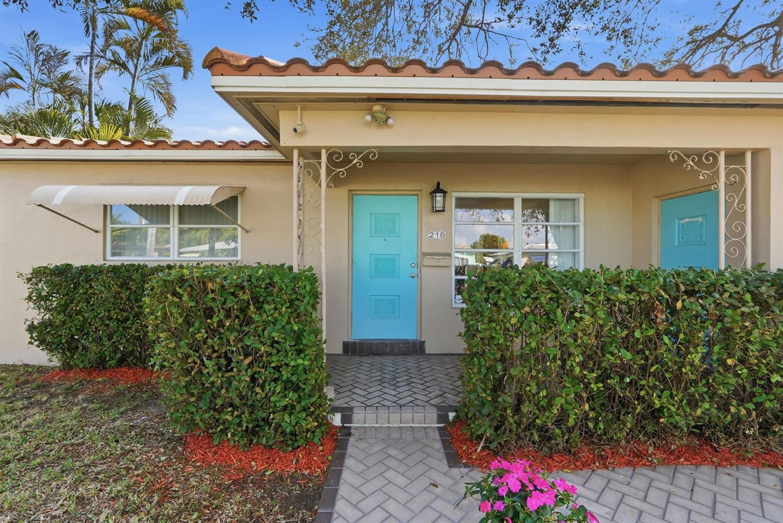 The exterior of a single-story home features a bright blue door and a hedge — 218 SE 3rd Terrace, Dania Beach FL 33004, DANIA BEACH, FL