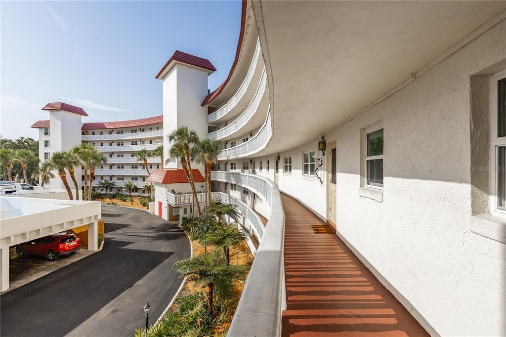 An exterior view of a curved apartment building featuring open-air walkways and a parking area — 601 N MCDONALD STREET UNIT 310, MOUNT DORA, FL