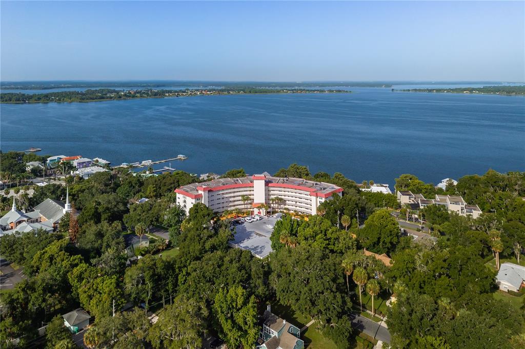 An aerial view shows a curved multi-story apartment building situated near a large lake — 601 N MCDONALD STREET UNIT 310, MOUNT DORA, FL