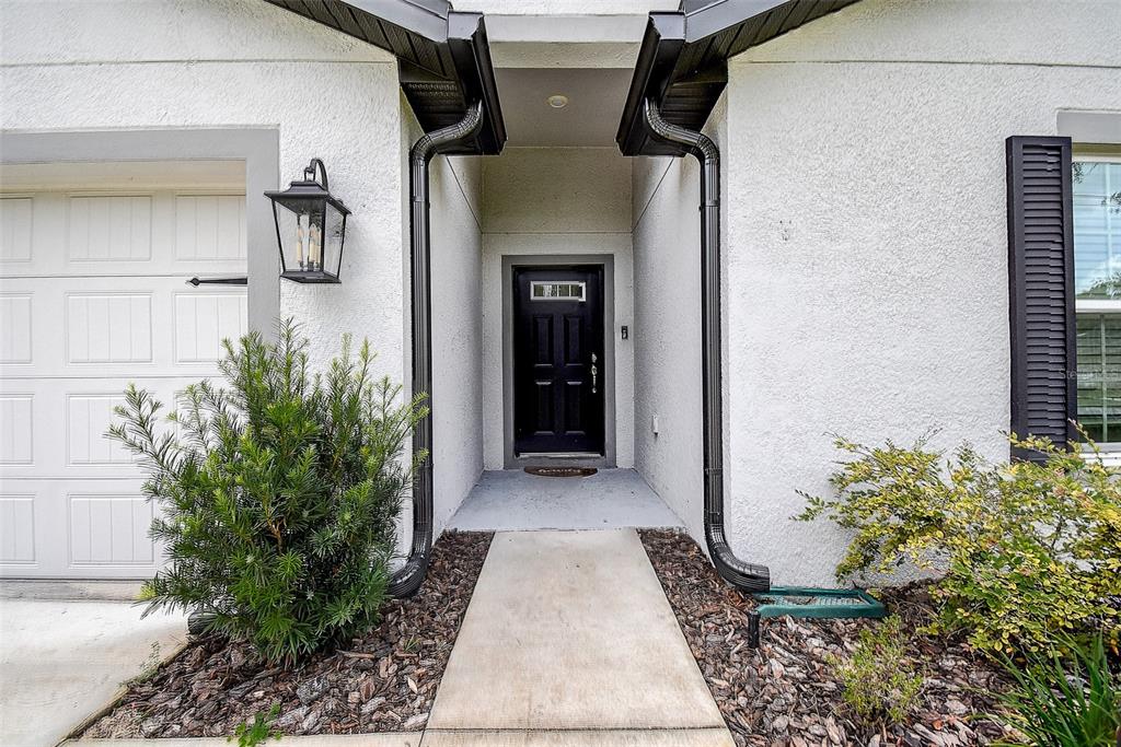 The exterior of a home features a black front door, a concrete walkway, and landscaping — 11014 GOLDEN WARBLER, BROOKSVILLE, FL