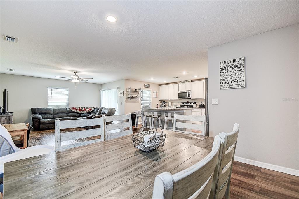 A dining area opens into a kitchen and living room with wood-look flooring — 11014 GOLDEN WARBLER, BROOKSVILLE, FL