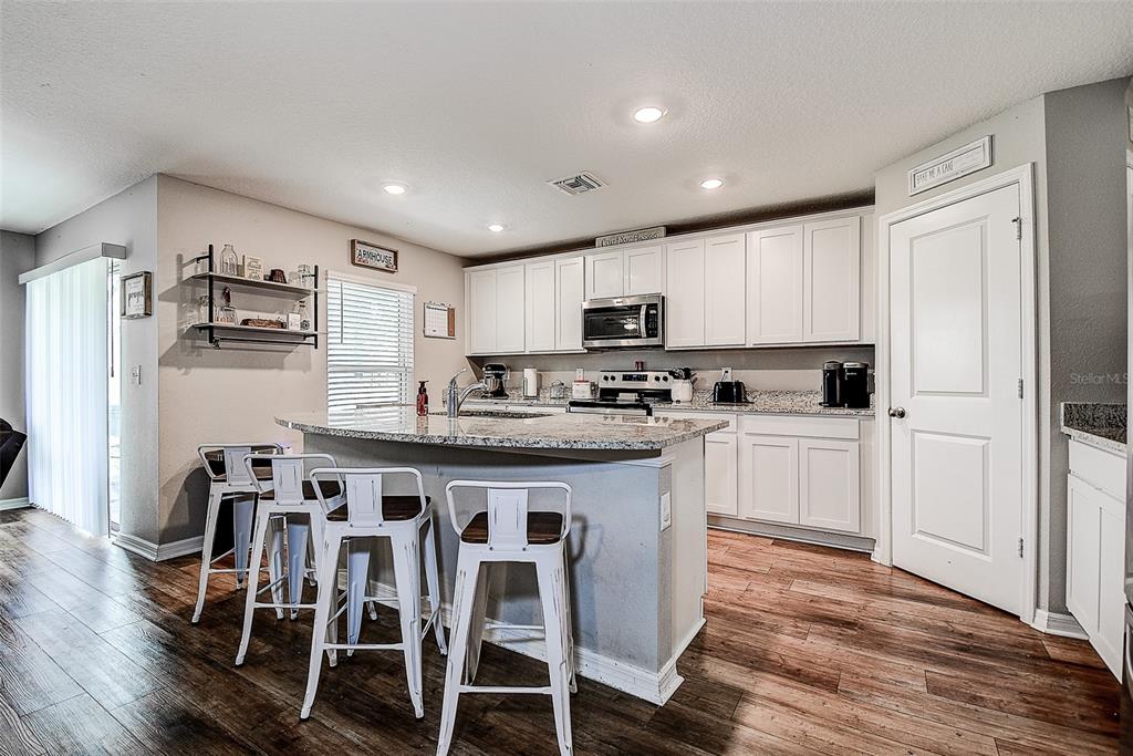 A kitchen features white cabinets, granite countertops, a center island with bar stools, and wood-look flooring — 11014 GOLDEN WARBLER, BROOKSVILLE, FL