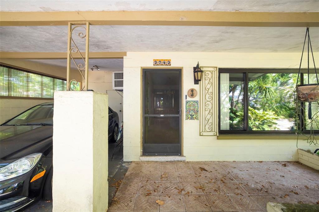 A covered porch features a screen door, a tiled floor, and a car parked nearby — 2742 S EAST AVENUE, SARASOTA, FL