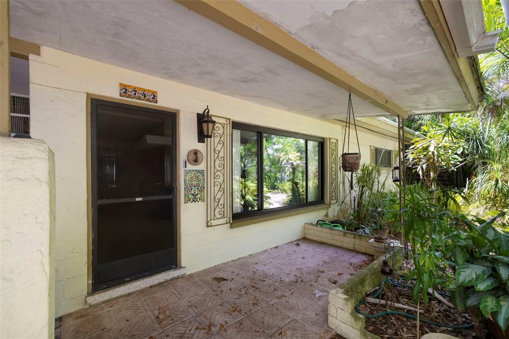 A covered porch with tiled flooring, a front door, a large window, and garden planters — 2742 S EAST AVENUE, SARASOTA, FL