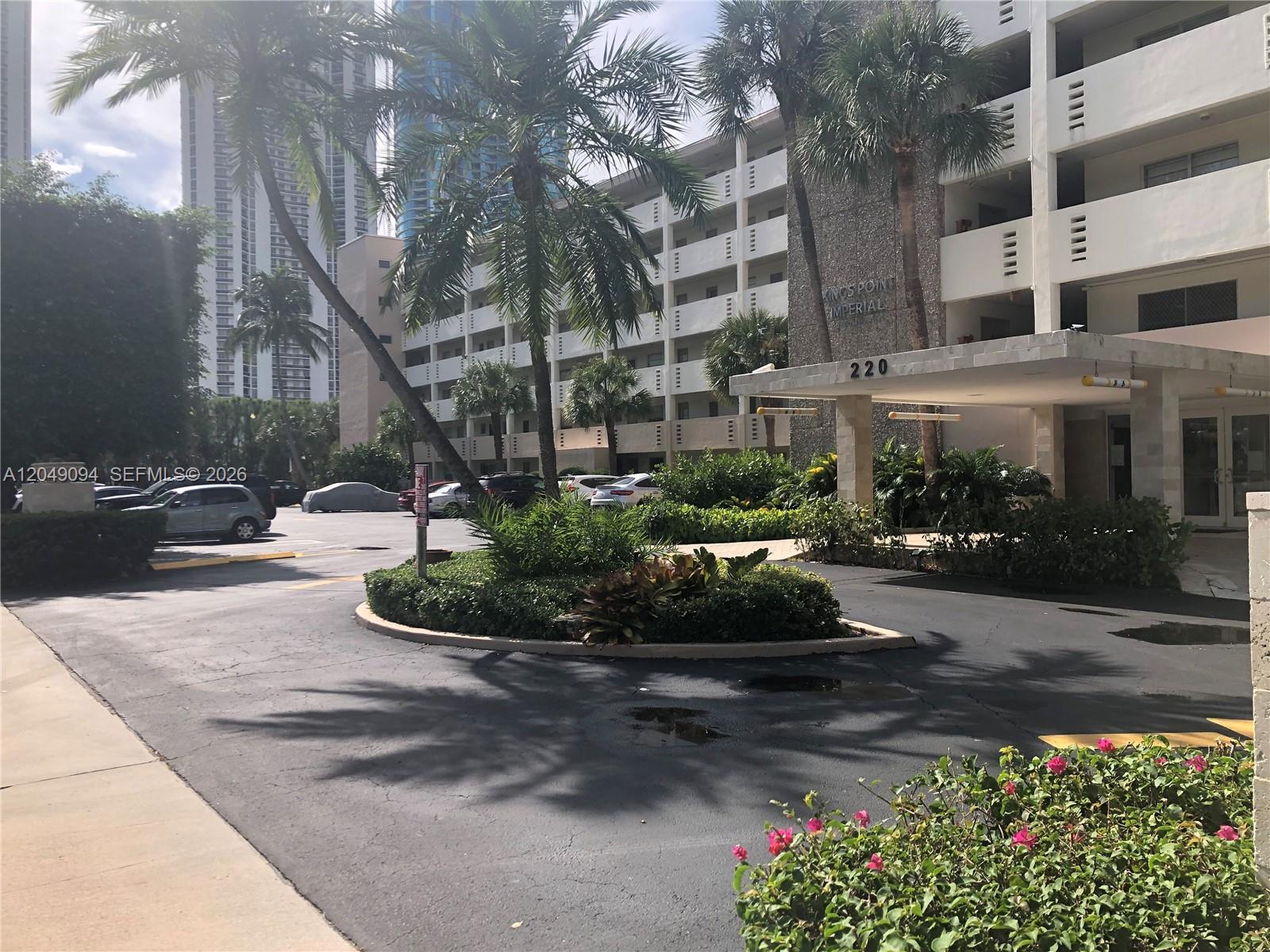 The exterior of a multi-story apartment building features a circular driveway and palm trees — SUNNY ISLES BEACH, FL