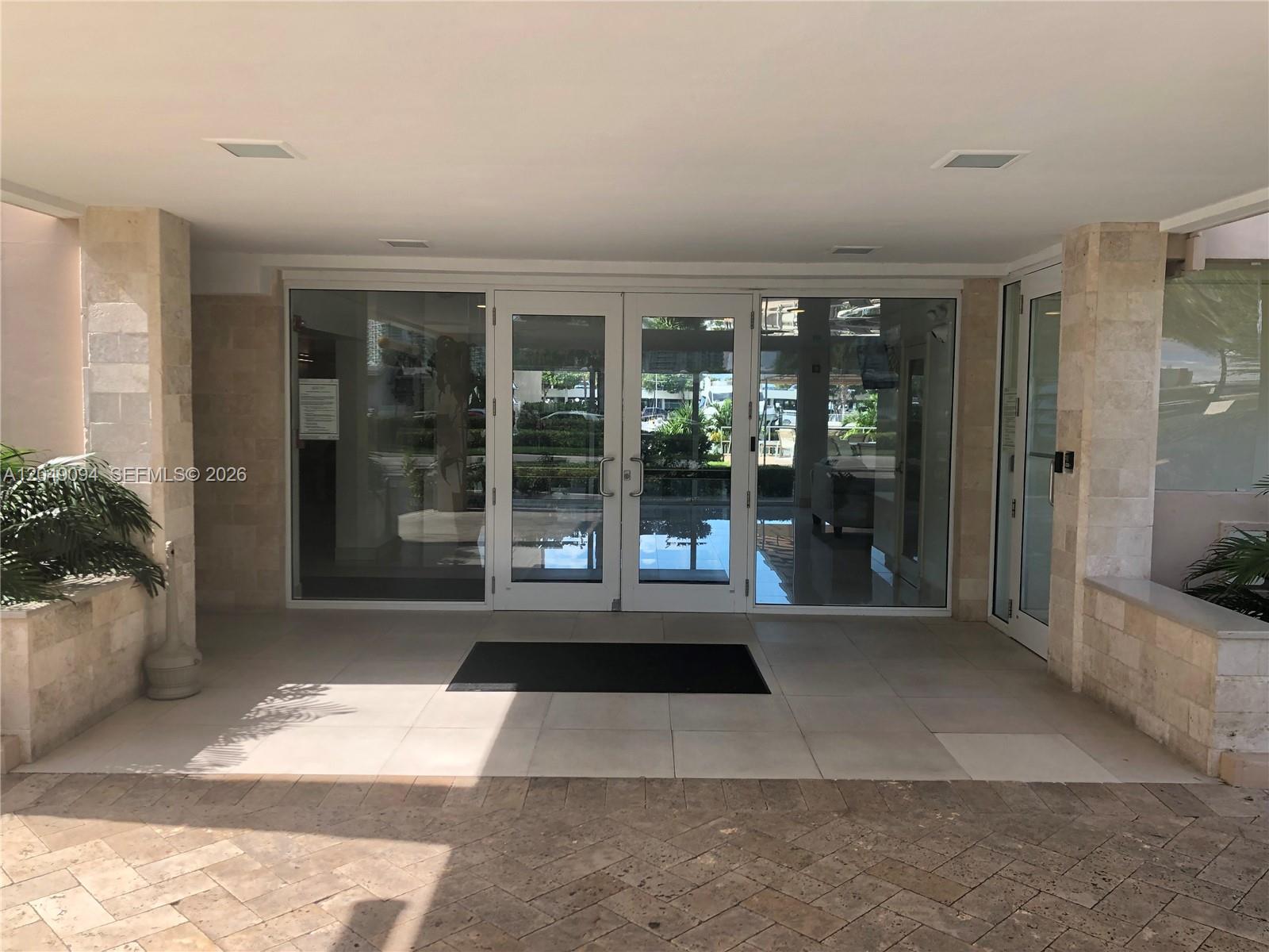 The exterior entrance features glass double doors framed by stone pillars and tiled flooring — SUNNY ISLES BEACH, FL