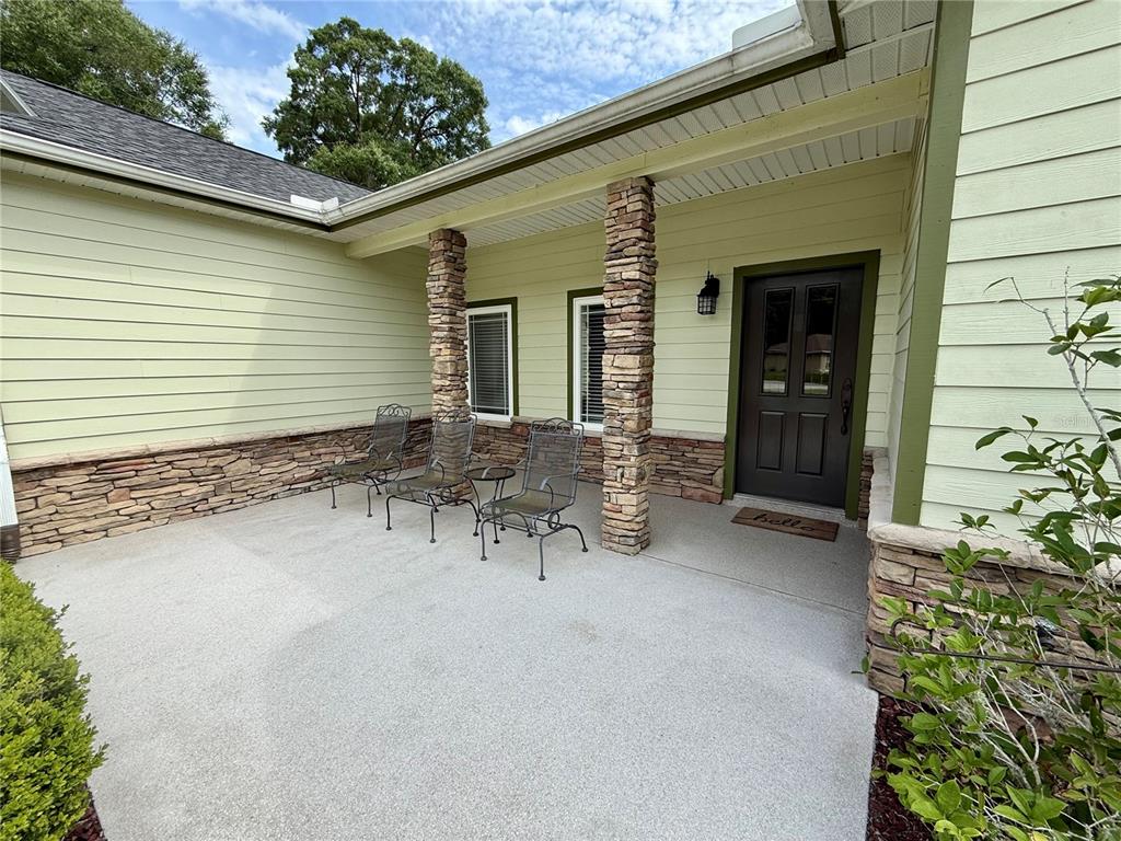 A covered front porch features stone columns, light green siding, and three metal chairs — 18450 NE 61ST LANE, WILLISTON, FL