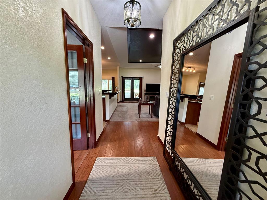 A hallway with wood floors leads toward a living area featuring a large decorative mirror — 18450 NE 61ST LANE, WILLISTON, FL