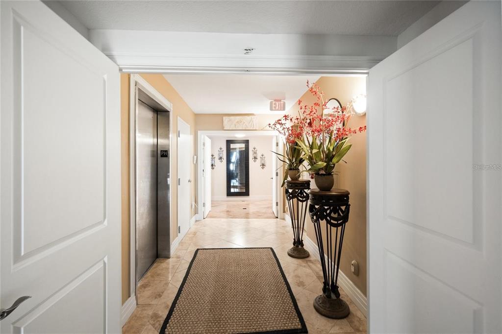 A hallway features a tile floor, an elevator, and two decorative pedestals with floral arrangements — 1350 GULF BOULEVARD UNIT 901, CLEARWATER BEACH, FL