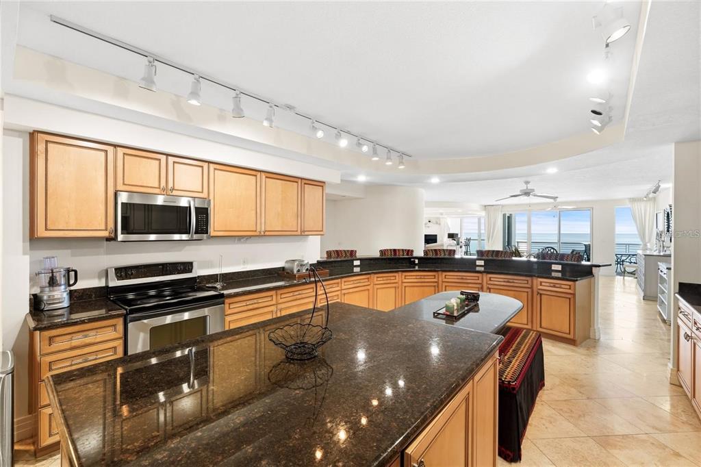 A kitchen with light wood cabinets, dark granite countertops, and a large curved island — 1350 GULF BOULEVARD UNIT 901, CLEARWATER BEACH, FL