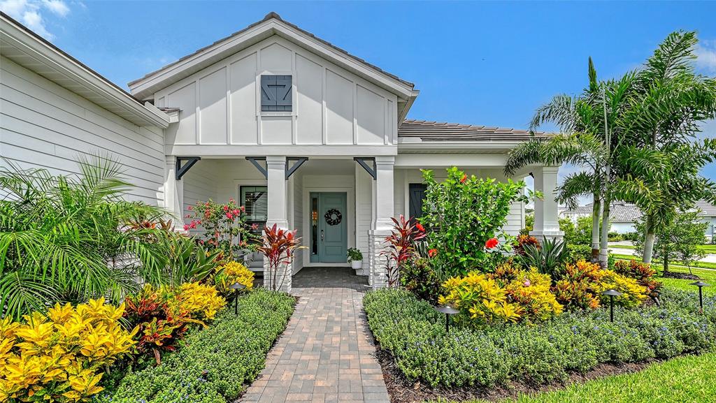 A white house with a blue front door features a landscaped walkway and palm trees — 2469 PARADISE PLUM DRIVE, SARASOTA, FL