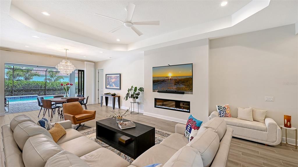 A living room with a fireplace, wall-mounted television, and an adjacent dining area with pool views — 2469 PARADISE PLUM DRIVE, SARASOTA, FL