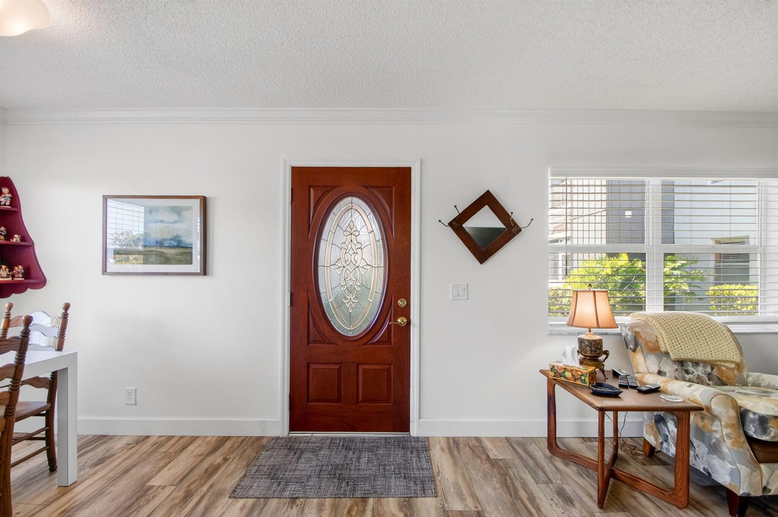 A living room features a wooden front door, light wood flooring, and a patterned armchair — 3 Normandy A, Delray Beach FL 33484, DELRAY BEACH, FL