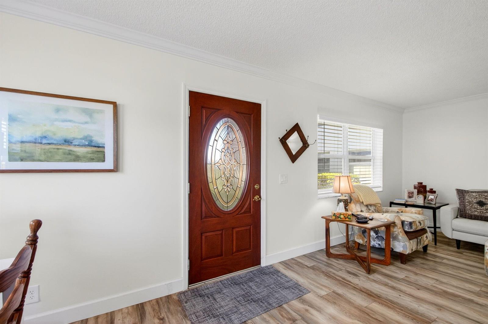 A living room features a wood-paneled front door, light wood flooring, and a patterned armchair — 3 Normandy A, Delray Beach FL 33484, DELRAY BEACH, FL