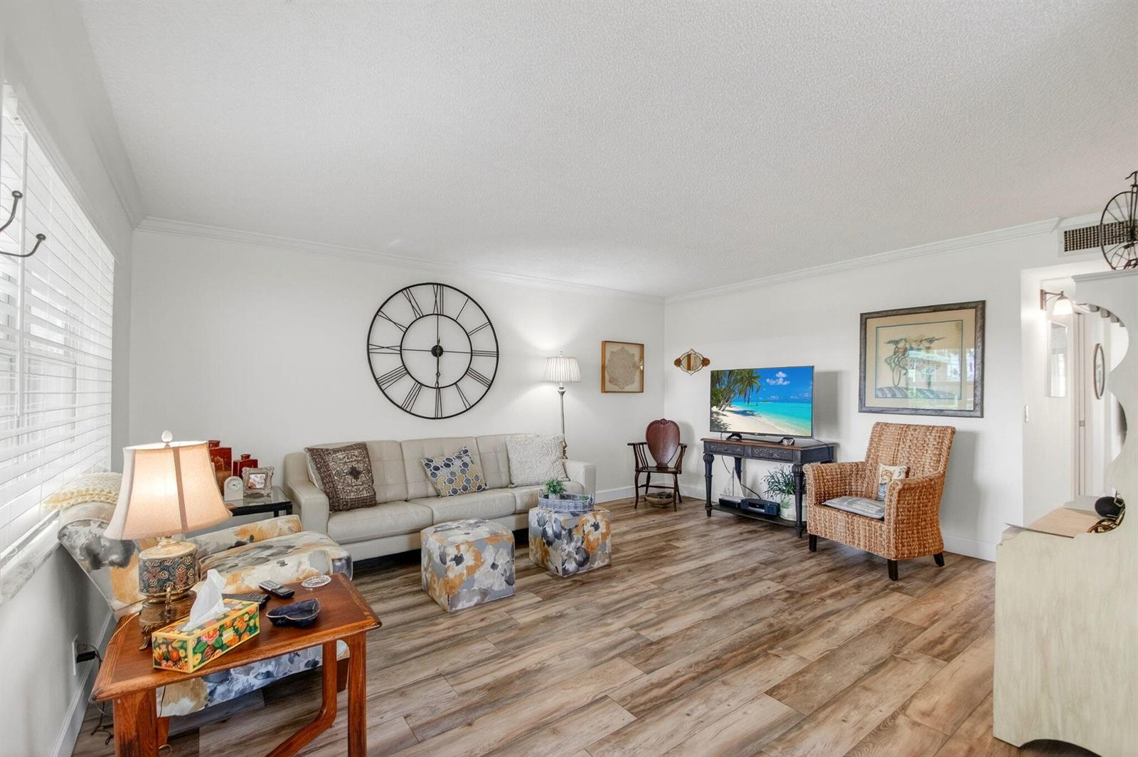 A living room features a beige sofa, two patterned ottomans, a television, and wood-look flooring — 3 Normandy A, Delray Beach FL 33484, DELRAY BEACH, FL