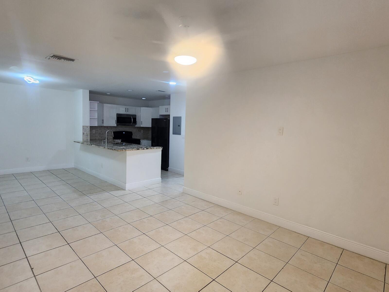 An open-concept living area features light-colored tile flooring and a kitchen with granite countertops — 6013 10th Avenue N # 208, FL 33463, FL