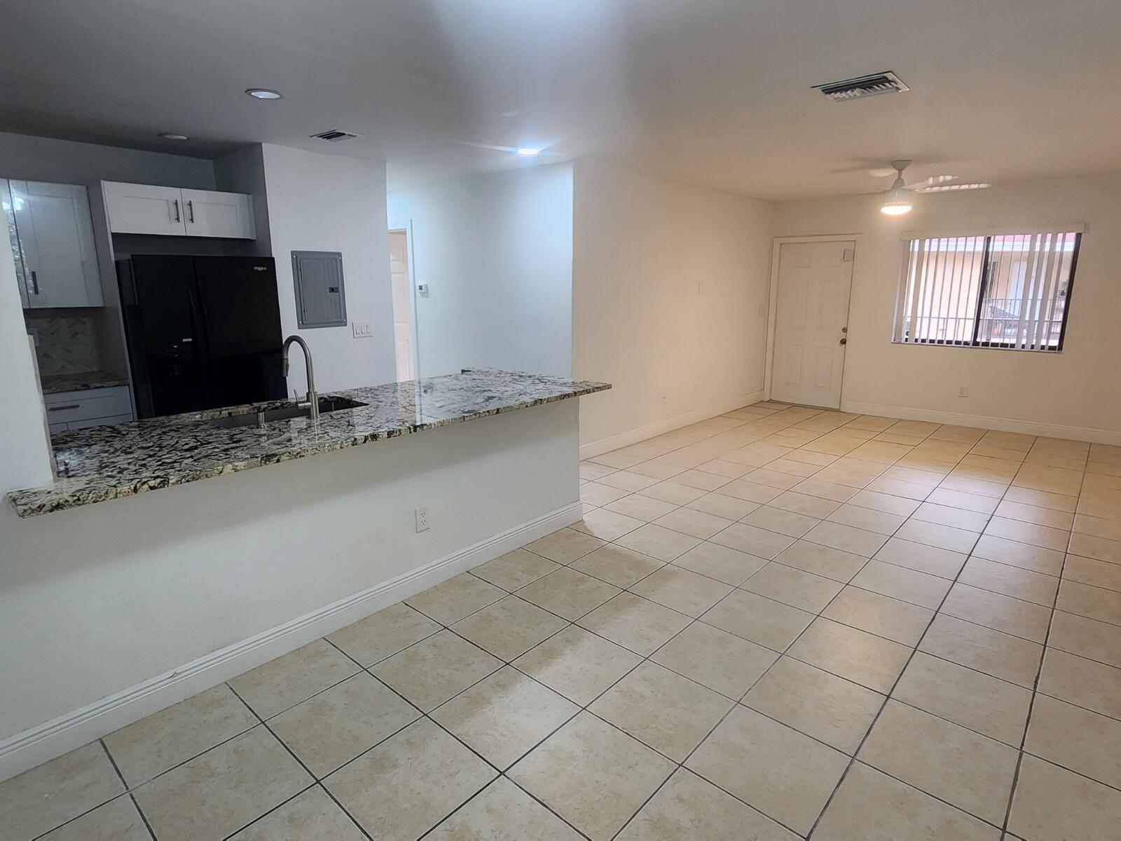 An open-concept kitchen with granite countertops and tile flooring flows into a living area — 6013 10th Avenue N # 208, FL 33463, FL